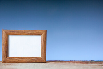 Close up view of brown empty picture frame standing on table on the right side on blue wave background