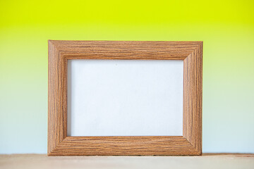Close up view of brown empty picture frame standing on table on yellow white mix color background