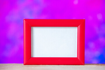 Close up view of red empty picture frame standing on white table on blue abstract mixed paint background with free space