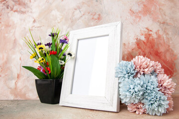 Close up view of white empty wooden photo frame and beautiful flowers on mixed colors background