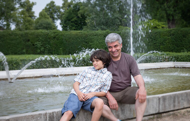 Dad and son are relaxing in the city park near fountains. Family have fun. Happy fathers day.