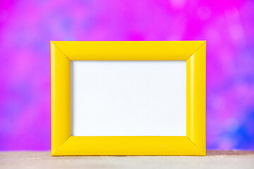 Close up view of yellow empty picture frame standing on table on purple and blue background with free space