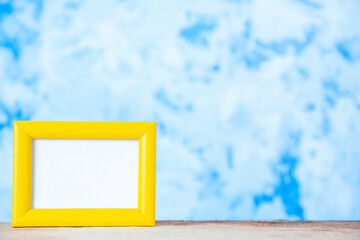 Close up view of yellow empty picture frame standing on table on the right side on blue watercolor texture background with free space