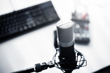 Broadcast, live stream, talk, voice recording, DJ, webinar, concept.  A large condenser microphone mounted on a mic holder with a stand. PC, mouse, and mixer on table.  Shallow depth of field.