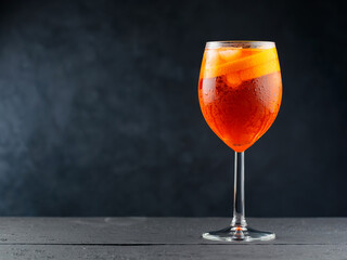 Aperol Spritz cocktail in glass with fresh orange on dark wooden boards. Glass of Aperol Spritz cocktail served in a wine glass. Copy space