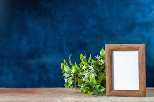 Front view of brown empty picture frame standing on table and flower on dark blue color background