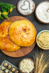Overhead view of delicous fresh baked pastries and cheese peppers eggs heart shaped flour on the wooden cutting board on dark blackground