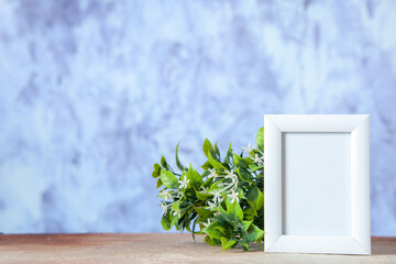 Top view of empty picture frame standing on table and flower pot on blue icy background