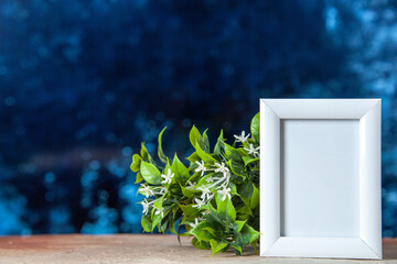Top view of empty picture frame standing on table and flower pot on dark blue color background