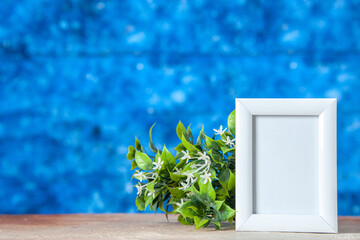 Top view of empty picture frame standing on table and flower pot on soft blue color background