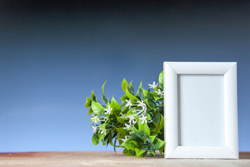 Top view of empty picture frame standing on table and flower pot on the right side on pastel blue colors background with free space