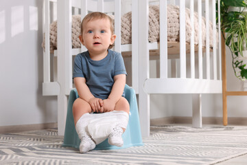 Little child sitting on plastic baby potty indoors. Space for text