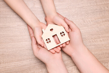 Home security concept. Man with his little child holding house model at wooden table, top view