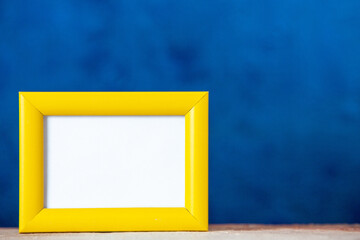 Top view of yellow empty picture frame standing on table on the right side on blue texture background with free space