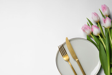 Stylish table setting with cutlery and tulips on white background, flat lay. Space for text