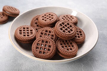 Tasty chocolate sandwich cookies with cream on light grey table