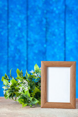 Vertical view of brown empty picture frame standing on table and flower on blue wooden background
