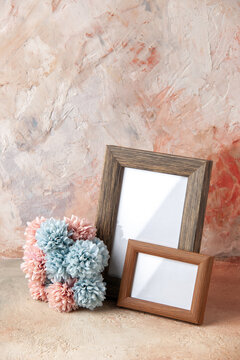 Vertical view of brown small and big empty wooden photo frames standing on table and flower on nude color background