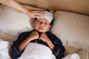 Boy gets high fever lying on bed with cold compress, wet washcloth on forehead. 