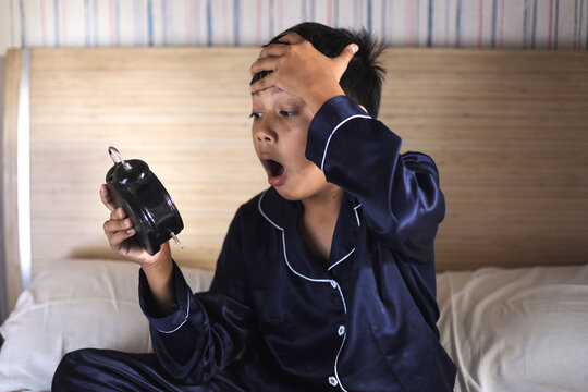 Worried awake teen boy with alarm clock is shocked because it is too late