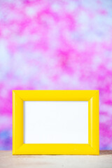 Vertical view of yellow empty picture frame standing on white table on colorful background with free space