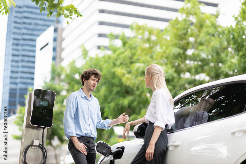 Wall mural progressive businessman and businesswoman with electric car parking and connected to public charging