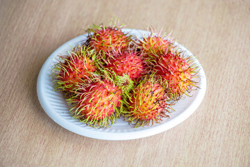 Top view of fresh ripe rambutans on plate on wooden background.