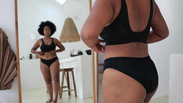 Variety of models with diverse types of face, body, race, gender. Plus size black polyethnic feminist body-positive female model in underwear in front of mirror flaunts her attractive healthy body.