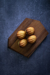 Freshly baked madeleine cakes on a wooden plate and dark table - 600014528