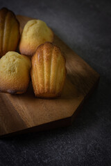 Freshly baked madeleine cakes on a wooden plate and dark table - 600014560