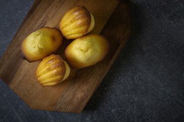 Freshly baked madeleine cakes on a wooden plate and dark table - 600014561
