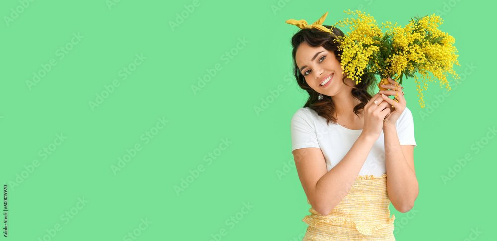 Wall mural Beautiful young woman with bouquet of mimosa flowers on green background with space for text