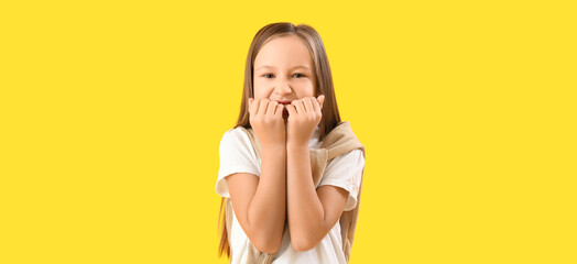 Little girl biting nails on yellow background