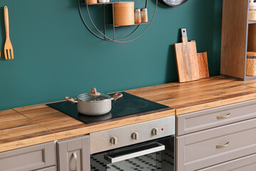 Electric stove with cooking pot and cutting board on kitchen counter near green wall