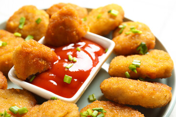 Plate with delicious nuggets, bowl of ketchup and cut green onion, closeup