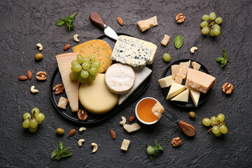 Different types of tasty cheese, honey, nuts and grapes on dark background