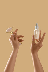 Hands holding cosmetic product and massage tool on beige background