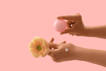 Hands holding jar of cream and flower on pink background