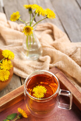 Board with glass cup of healthy dandelion tea on wooden background