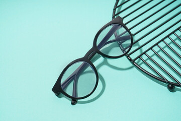 Black modern eyeglasses and stand on pale turquoise background
