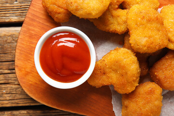 Board with delicious nuggets and bowl of ketchup on wooden table, closeup