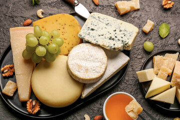 Tray with different types of tasty cheese and grapes on dark background