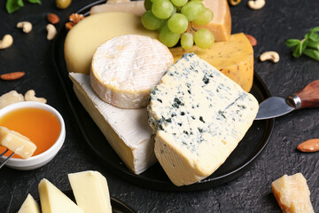 Tray with different types of tasty cheese on dark background