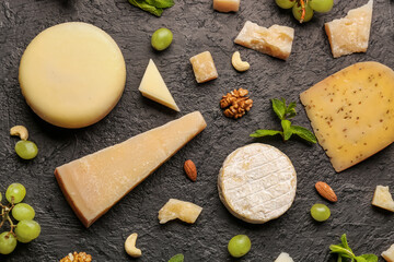 Different types of tasty cheese, grapes and nuts on dark background