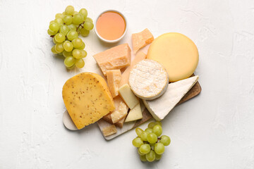 Board with different types of tasty cheese, grapes and honey on light background