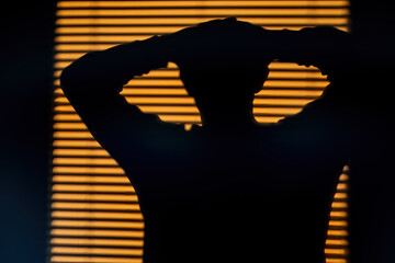 A man's shadow is projected onto a wall and window blinds at sunrise.
