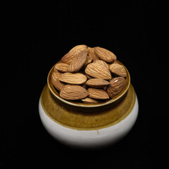 closeup shot of fresh brown almonds filled up and stored in a traditional pot jar isolated in a black background