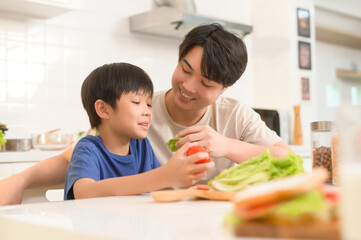 Obraz na płótnie Canvas Happy Young Asian father and son eating healthy food in kitchen at home