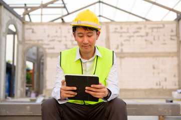 An Asian engineer man is wearing a protective helmet on head, using tablet Analytics engineering data