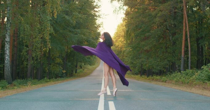 Fantasy graceful flexible woman queen dancing holding purple cloth in hands Silk purple fluttering flying in wind. Dancer in a black body suit twirls around as fabric flutters with the movement